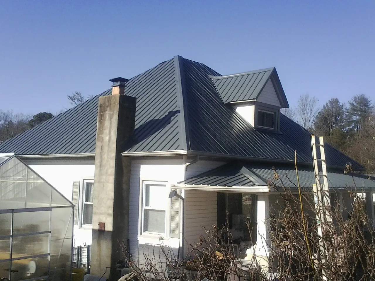 Dark blue standing seam metal roof on a white farmhouse with dormer — Slate & Tile Roof Repair by Roofing Brothers in Dahinda