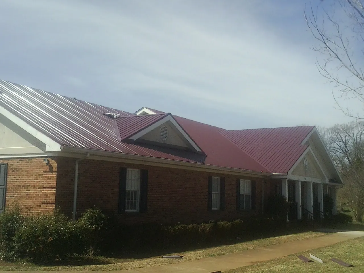 Red metal roof with gabled entries on a long brick building, from a Hail Damage Roof Repair job in Dahinda