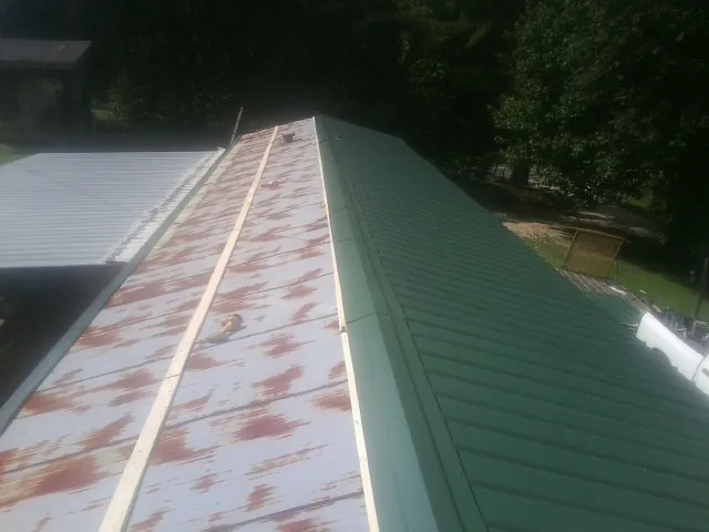Old rusted panels beside newly installed green metal roofing — Wind Damage Roof Repair by Roofing Brothers in Dahinda