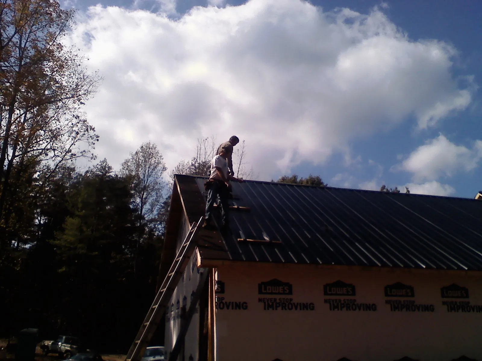 Roofer fastening dark metal panels high against a cloudy sky, from a Roof Inspection job in Dahinda
