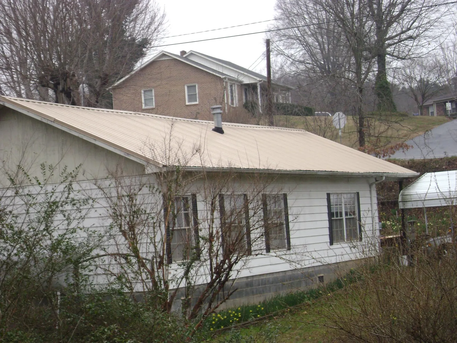 Tan metal roof on a white sided house set into a hillside — Commercial Roofing by Roofing Brothers in Dahinda